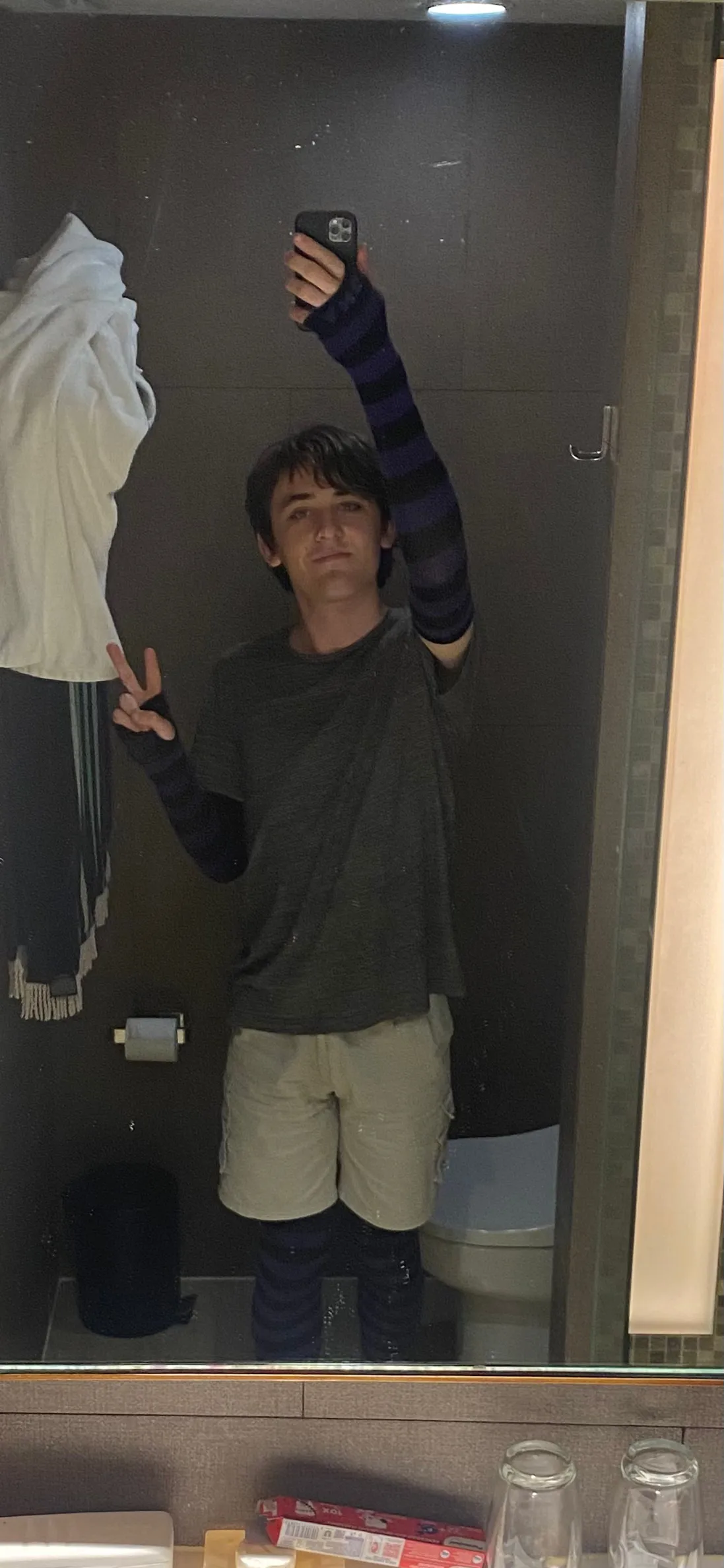A photo of a person wearing purple and black socks and arm warmers, holding their phone above their head to take a photo of themself in the mirror of a Balinese hotel bathroom. How gay is that?