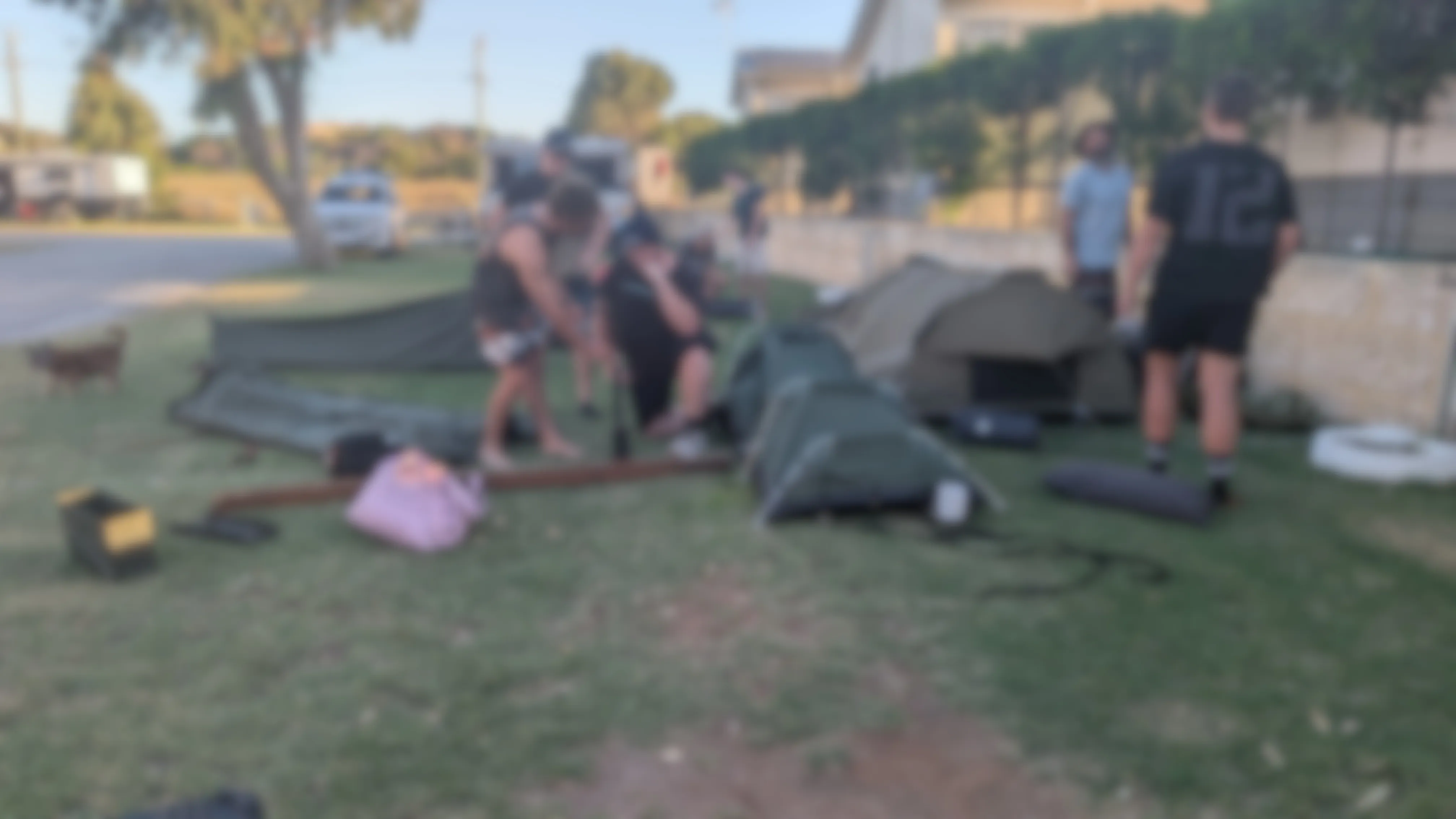 A blurred photo of people setting up swags at a campsite