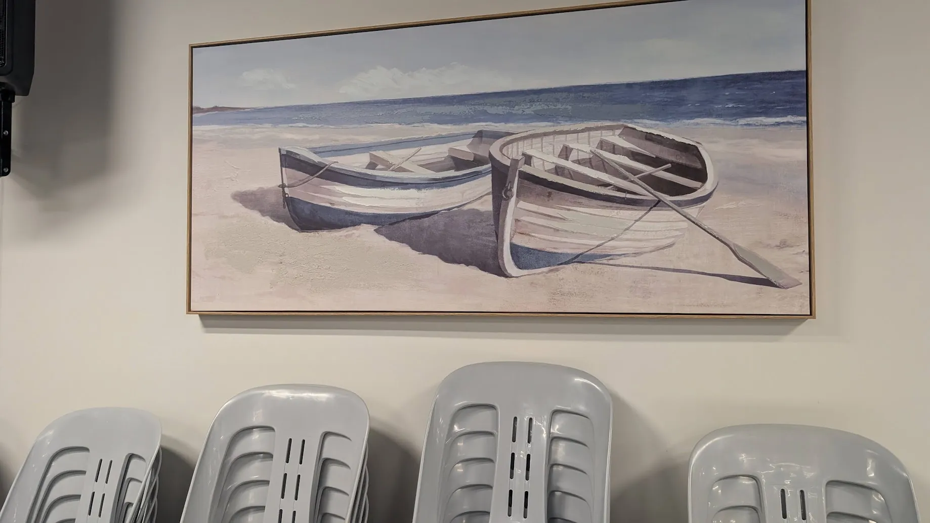 A photo of a painting of two boats on a wall above a stack of chairs.