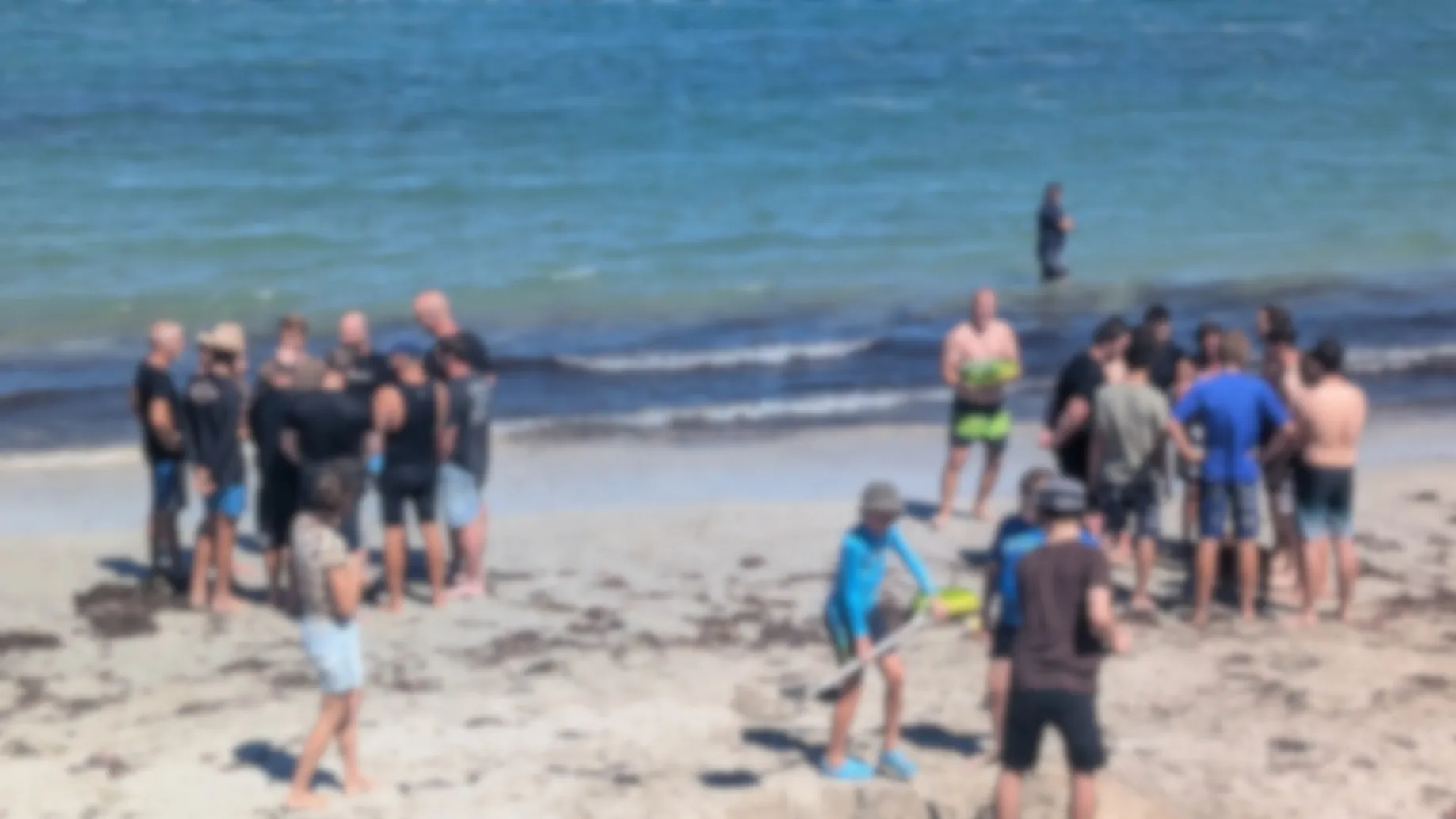 A blurred photo of a group of people huddled into two teams on a beach.