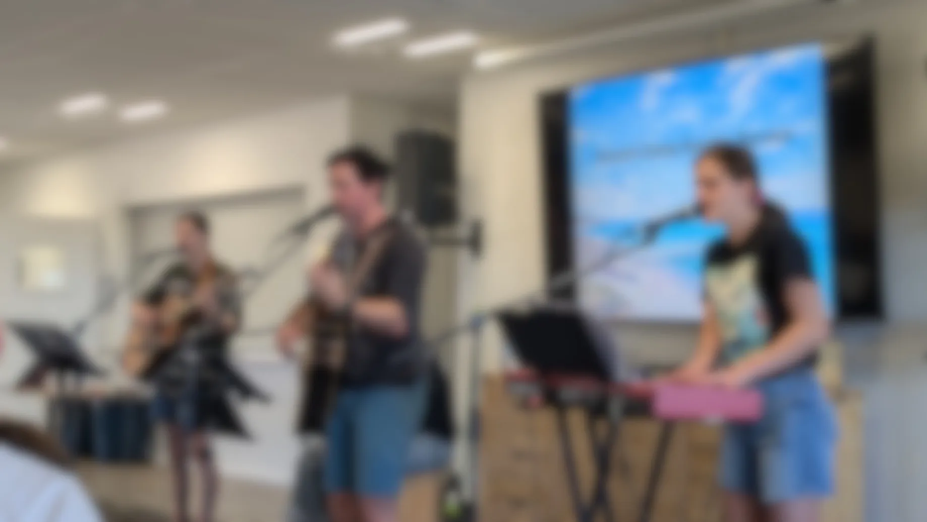 A photo of three people singing whilst playing the guitar and piano