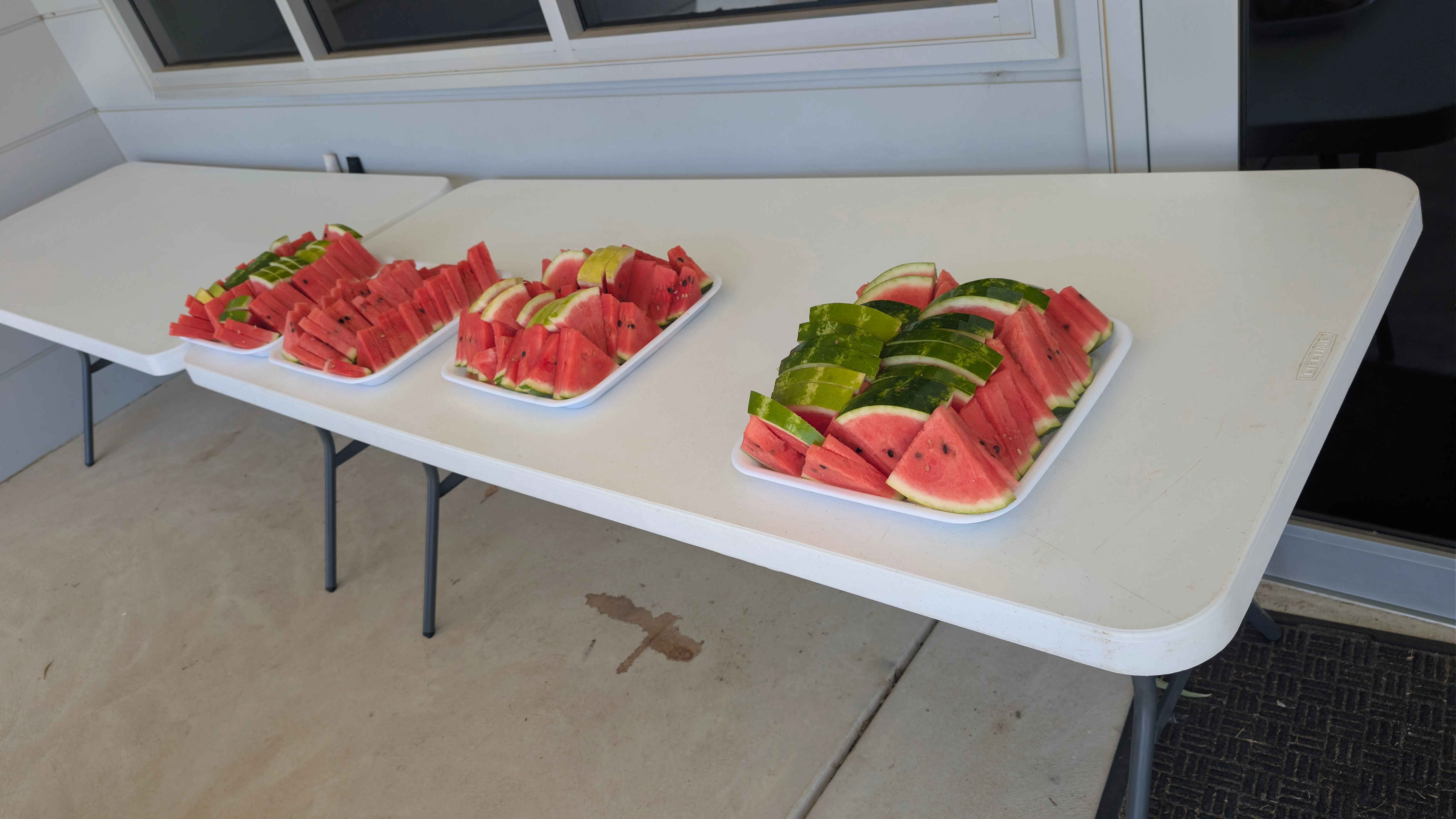 A photo of four trays of sliced watermelon displayed on a table.